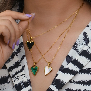 Three layered gold necklaces with black, green, and white heart pendants on model