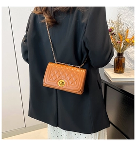 Detail of caramel quilted square bag with gold twist lock and fine chain strap on model