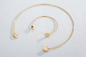 Close-up of gold titanium steel jewelry set featuring heart and cross charms on textured white