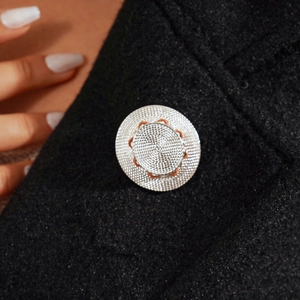 Macro shot of silver metal straw hat brooch with detailed mesh texture on a black blazer