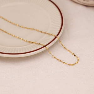 Minimalist gold O-link chain necklace displayed on a white ceramic plate