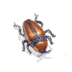 Detailed macro view of an orange enamel beetle brooch with black zircon embellishments