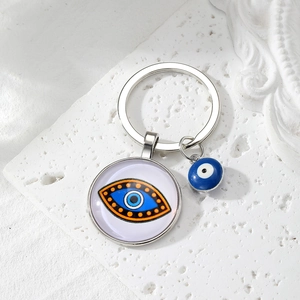 Close-up of silver Evil Eye keychain with glass pendant and blue bead on stone surface