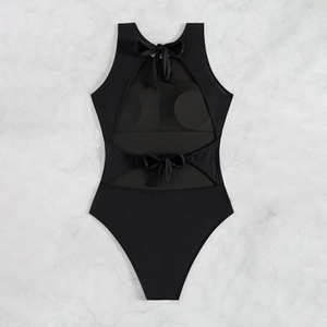 Back view of black one-piece swimsuit with cutout design and bow ties on marble background