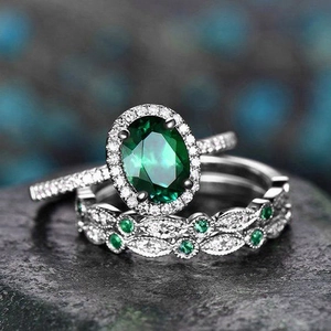 Macro shot of oval emerald green gemstone ring set with halo diamonds on dark stone