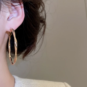 Detail of twisted gold metal hoop earring with textured finish on model's ear