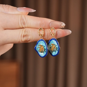 Detail of vintage-style gold earrings with blue floral enamel petals and gold stamens