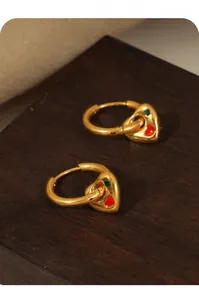 Detail of gold-plated heart earrings with red enamel and zircon on a wooden base