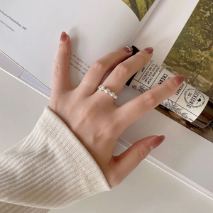 Detail of silver beaded ring with clear zircon worn against a cream knit background