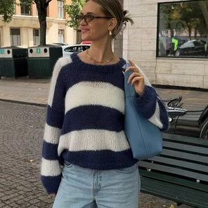 Women's oversized blue and white striped knit sweater paired with denim jeans and handbag