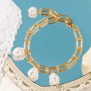 Detailed macro of gold rectangular link chain with five baroque pearls on mirror surface