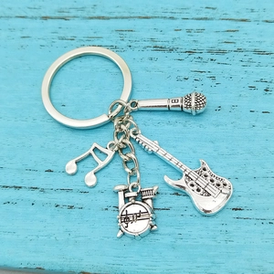 Silver music keychain with microphone guitar note and drum charms on blue wood