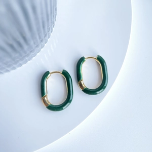 Detailed view of U-shaped gold earrings with green enamel on a white podium