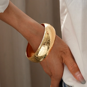 Close-up of golden wide cuff bracelet featuring detailed crocodile skin scale texture