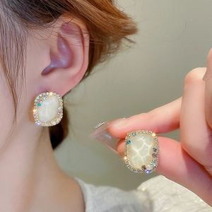 Close-up of vintage gold studs with cream square stones and colorful crystals