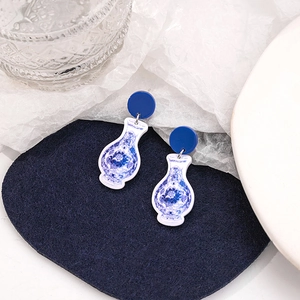 Macro detail of blue and white porcelain bottle earrings on a dark blue felt surface