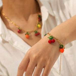 Detailed close-up of golden fruit charms on a stainless steel necklace and bracelet set