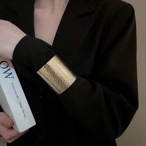 Close-up of hammered gold wide cuff bracelet worn over a black blazer sleeve