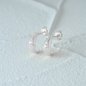 Close-up of silver C-shaped star stud earrings with micro-set zircon stones on white texture
