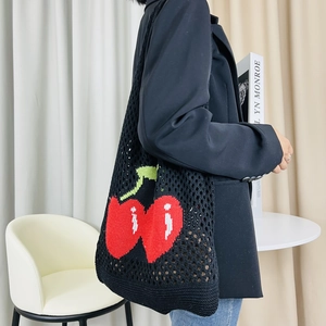 Close-up of black hollow knit tote bag with red cherry pattern on a fashion model