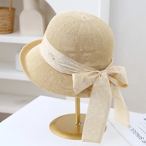 Close-up of beige woven sun hat with floral ribbon bow on a golden display stand