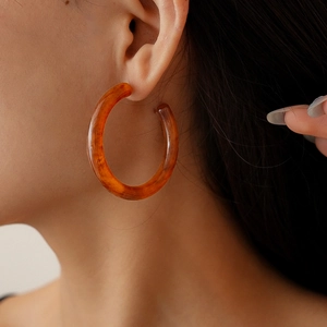 Close-up of amber resin C-shaped hoop earring on model showing warm translucent finish
