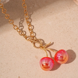 Gold chain necklace with red resin cherry charms and toggle clasp on stone surface