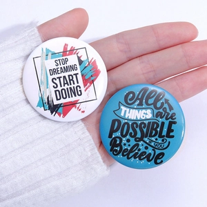 Detail of hand holding two round metal badges with motivational English quotes