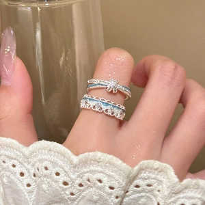 Detail of blue enamel flower ring and starburst band layered on a hand with lace