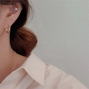 Detailed close-up of a 925 sterling silver gold hoop and white pearl stud set on an ear