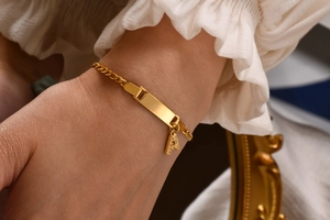 Close-up of golden stainless steel Cuban chain bracelet with letter A pendant and ID plate