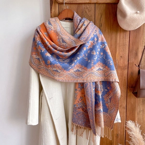 Ethnic paisley tassel shawl in blue and orange hanging against a white coat background