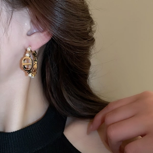 Close-up of gold-plated hoop earring featuring CD logo and white pearls on model