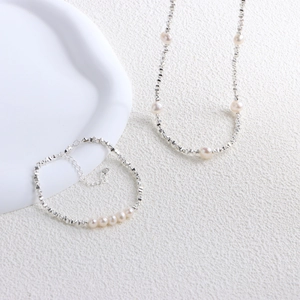 Detail view of irregular silver chain necklace and freshwater pearls on white tray