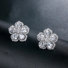 Close-up of silver floral stud earrings featuring five-petal zircon stones and metallic finish