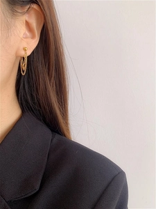 Detail view of gold layered tassel chain earrings on model with a black suit