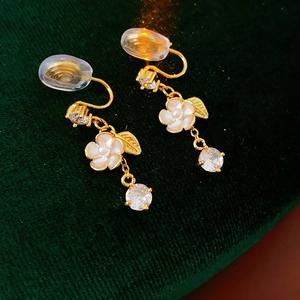 Close-up of gold flower clip-on earrings with zircon drops on green velvet
