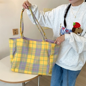 Macro detail of large plaid canvas tote bag showing yellow purple green grid and handle