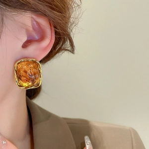 Close-up of amber resin square earring with gold twisted metal border on model