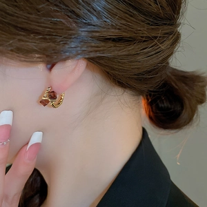 Detail view of gold twisted hoop earring with a square amber zircon on a model