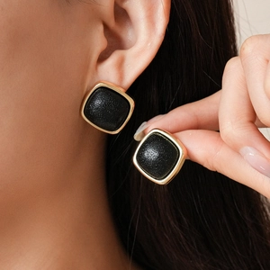 Close-up of vintage geometric square earrings featuring black leather texture and gold metal