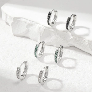 Detailed view of silver huggie earrings with black, green, and clear cubic zirconia