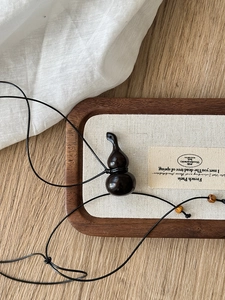 Detail view of a handcrafted dark wood gourd pendant with black beaded cord on a tray