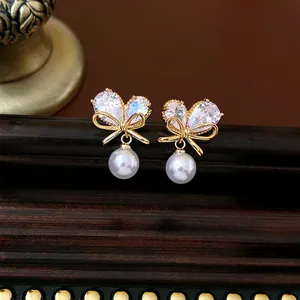 Boucles d'oreilles nœud doré avec zircons et perles sur un support en bois sombre