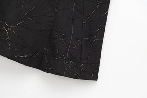 Close-up of black textured fabric with unique distressed pleated details and fiber lines