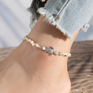 Close-up of a silver sea turtle charm on a beige woven rope anklet for beach fashion
