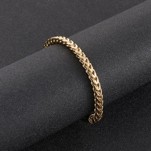 Détail d'un bracelet en maille épi dorée exposé sur un support cylindrique gris foncé