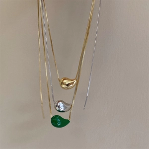 Detailed view of polished water-drop pendants in gold, silver and green on box chains