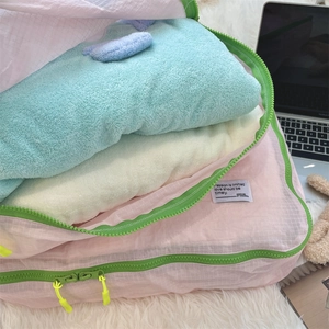 Detail view of pink grid travel organizer bag with green zippers on white plush carpet