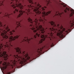 Detail of burgundy mesh fabric with black flocked floral patterns and mesh texture